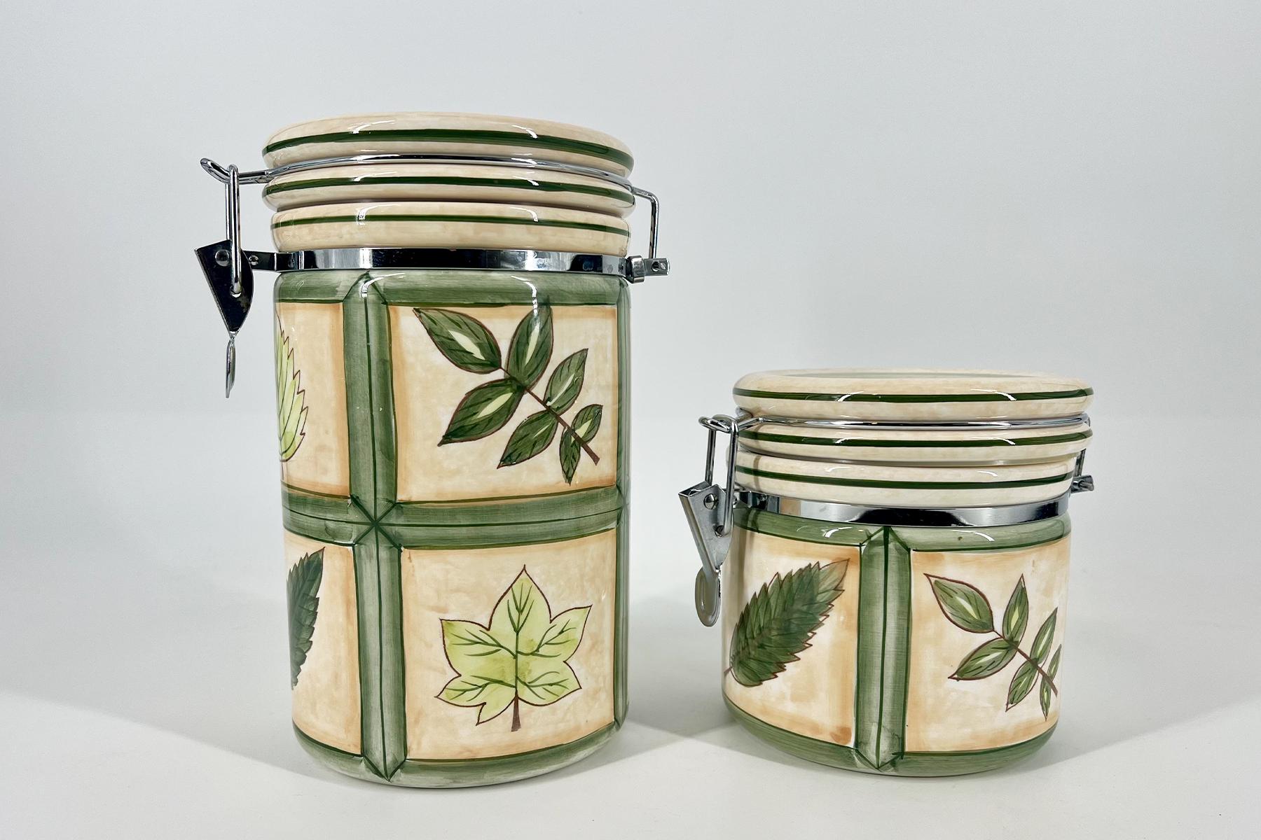 Two ceramic canisters with green leaf patterns and metal latch lids, set against a light background.