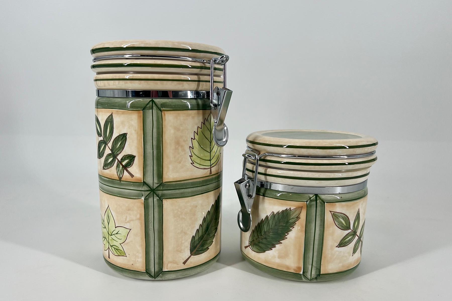 Two ceramic airtight canisters with metal clasps, tall and short, featuring green botanical patterns on a beige background against a light gray backdrop.
