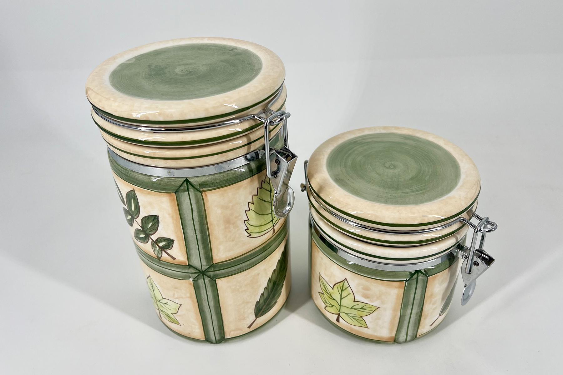 Stack of decorative ceramic drums with green rims and leafy patterns, metal clasps visible on lids, beige glaze.