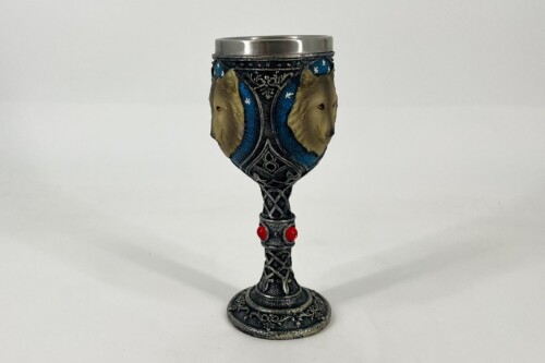 Ornate metal goblet with blue and black etched patterns, two wolf head reliefs on the sides, and red gemstone accents in the stem