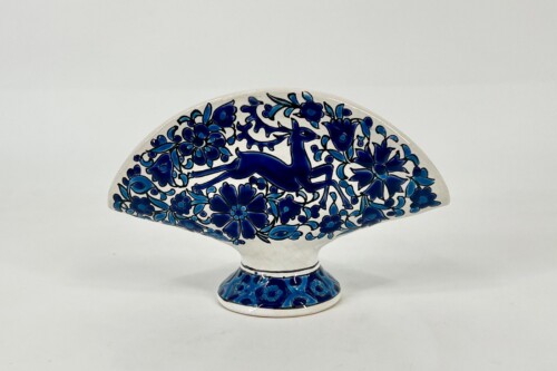 Blue-and-white decorative porcelain plate in a fan shape with a cobalt deer among flowers, displayed on a small pedestal base