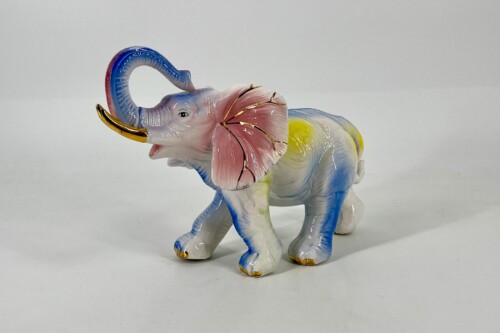 Colorful porcelain elephant figurine with a curved blue trunk and pink ears, standing on a white surface.