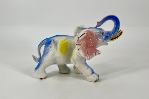 Colorful ceramic elephant figurine with a curled blue trunk and pink ears on a white surface, glossy finish.