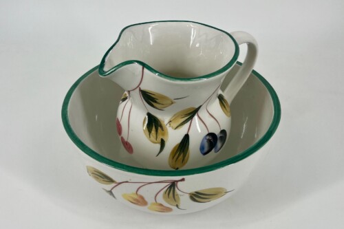 White ceramic pitcher with a green rim resting inside a matching bowl, both decorated with a yellow leaf and fruit pattern.