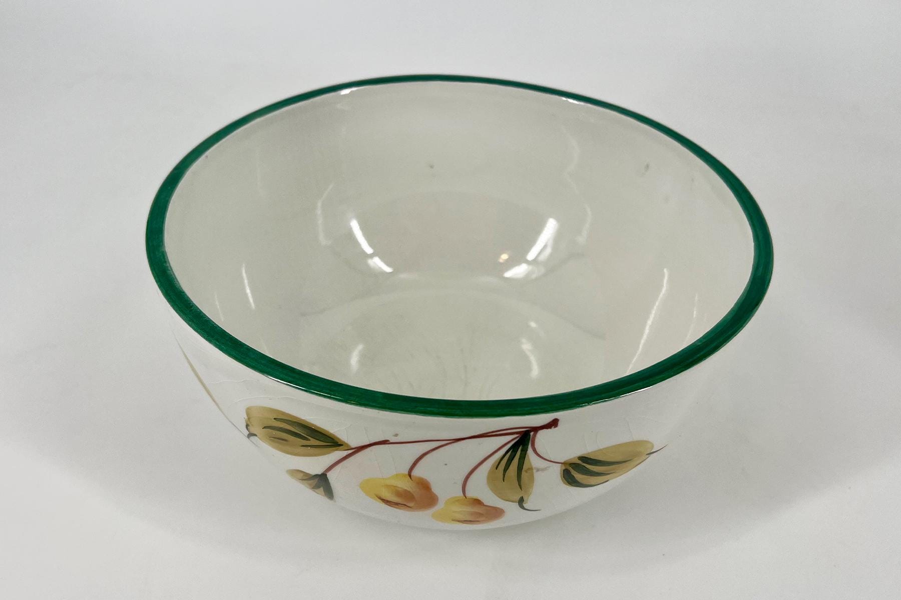 White porcelain bowl with a glossy white interior, green rim, and yellow floral pattern on the outside, viewed from above.