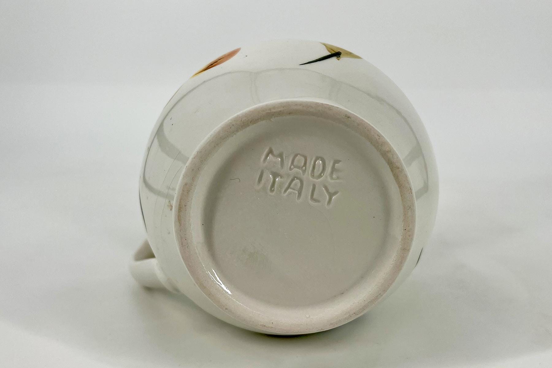 White ceramic mug on its side, bottom stamped with 'MADE IN ITALY'.