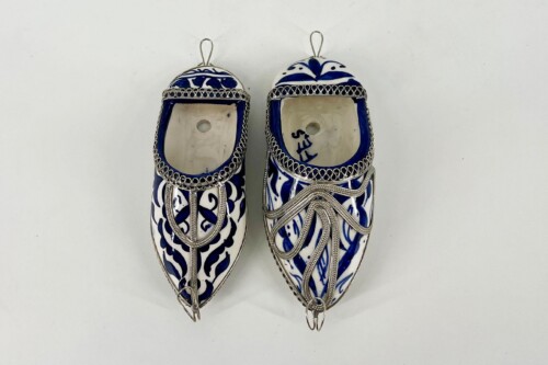 Two decorative blue-and-white porcelain slipper ornaments with silver filigree trim and hanging loops photographed side by side.