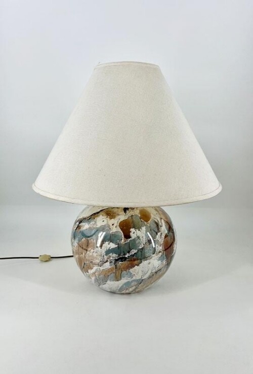 Table lamp with a round, marbled ceramic base in blue, brown, and white, topped by a beige fabric shade; cord extends to the left.