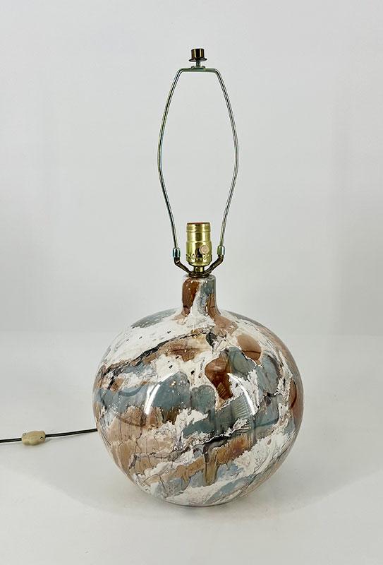 Round marbled ceramic lamp base with a brass socket and empty harp against a white backdrop.