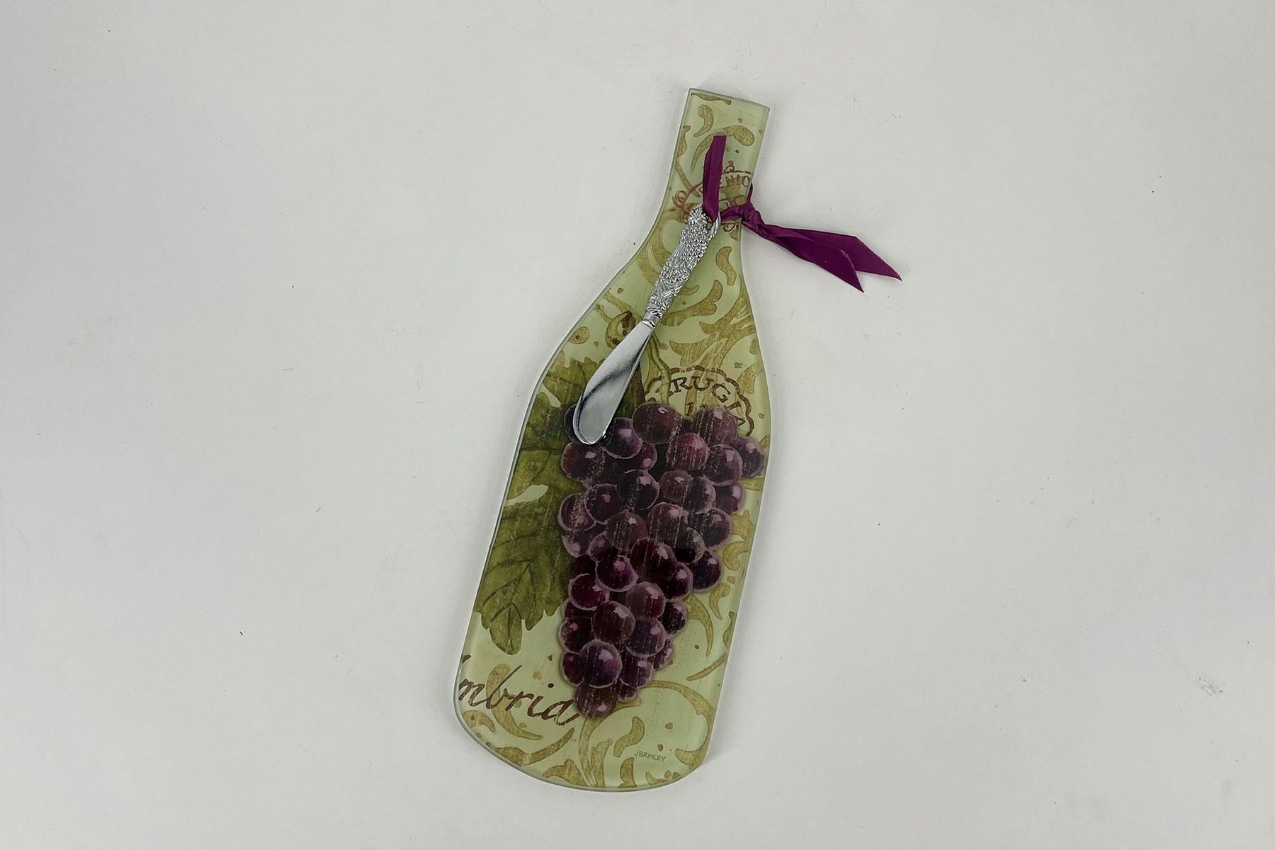 Decorative wine bottle-shaped board with a grape cluster design and a silver corkscrew tied with a purple ribbon at the neck