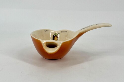 Orange ceramic gravy boat with a built-in spoon rest; interior shows 'HEAVY GRAVY' and a small carrot decoration in the center