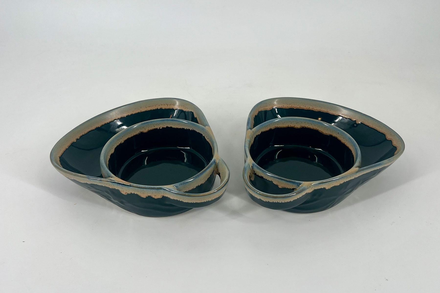 Two dark blue glazed ceramic bowls stacked side by side with rough beige rims on a white background.