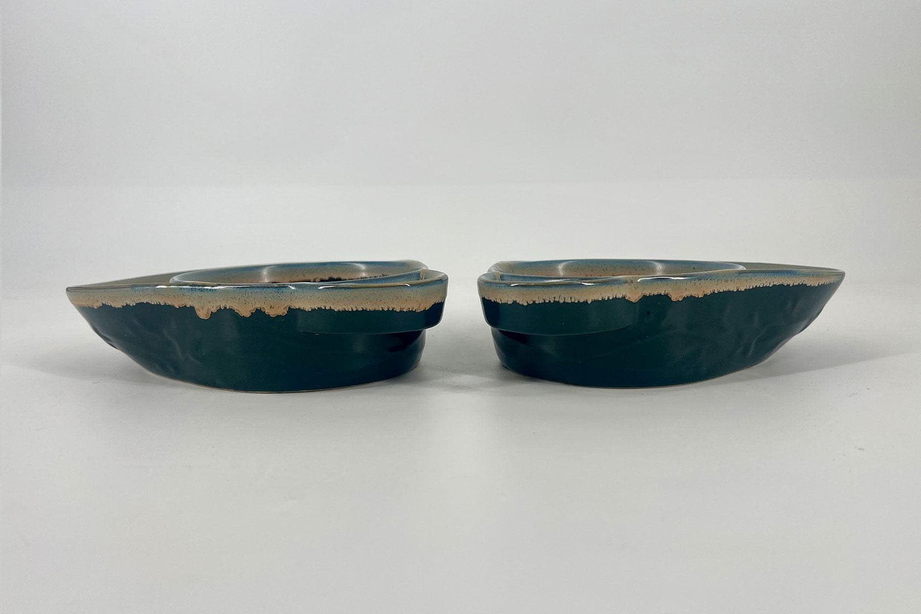 Pair of dark teal glazed ceramic bowls with a beige rim, placed side by side on a white surface.