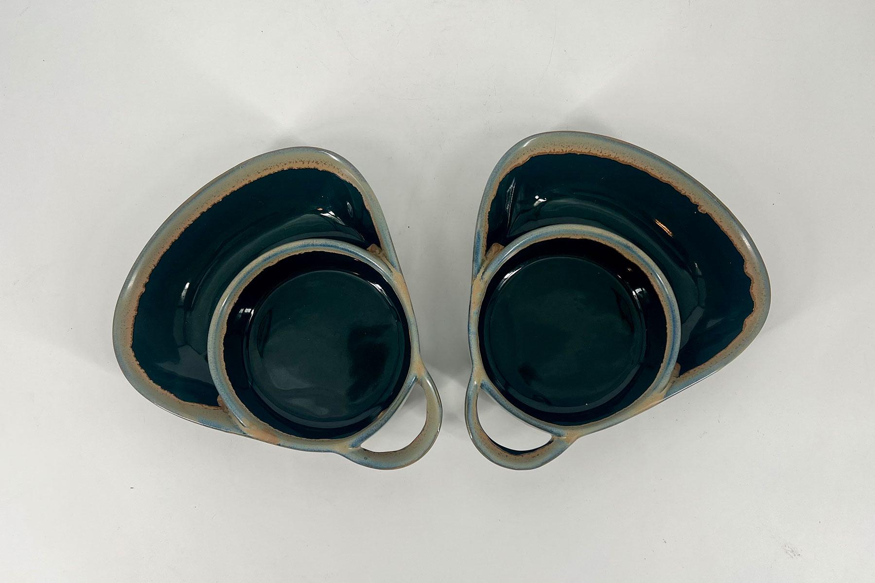 Pair of teal glazed ceramic nesting bowls with beige rims facing each other on a white surface.