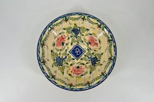 Decorative ceramic plate with a floral pattern, blue border, pink roses, grape clusters, and green vines on a yellow background.