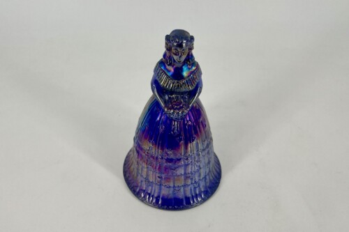 Iridescent glass figurine of a woman in a long pleated dress with hands folded in front.