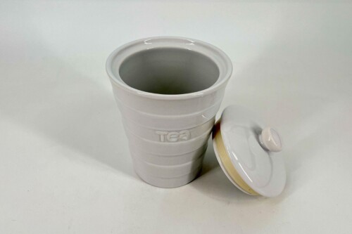 White ceramic tea mug with an open top and a lid resting beside it on a white surface.