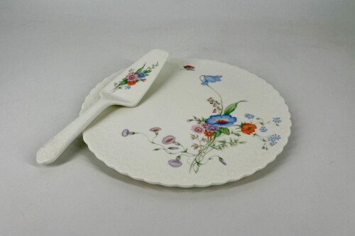 White porcelain plate with a scalloped edge and a colorful floral bouquet design, with a matching floral-patterned serving spatula laid across it.