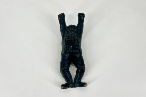 Small dark figurine of a human with arms raised overhead, standing on a flat base on a light background.