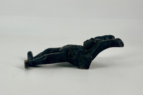 Dark patinated sculpture of a disembodied right hand resting on a light surface, viewed from the side.