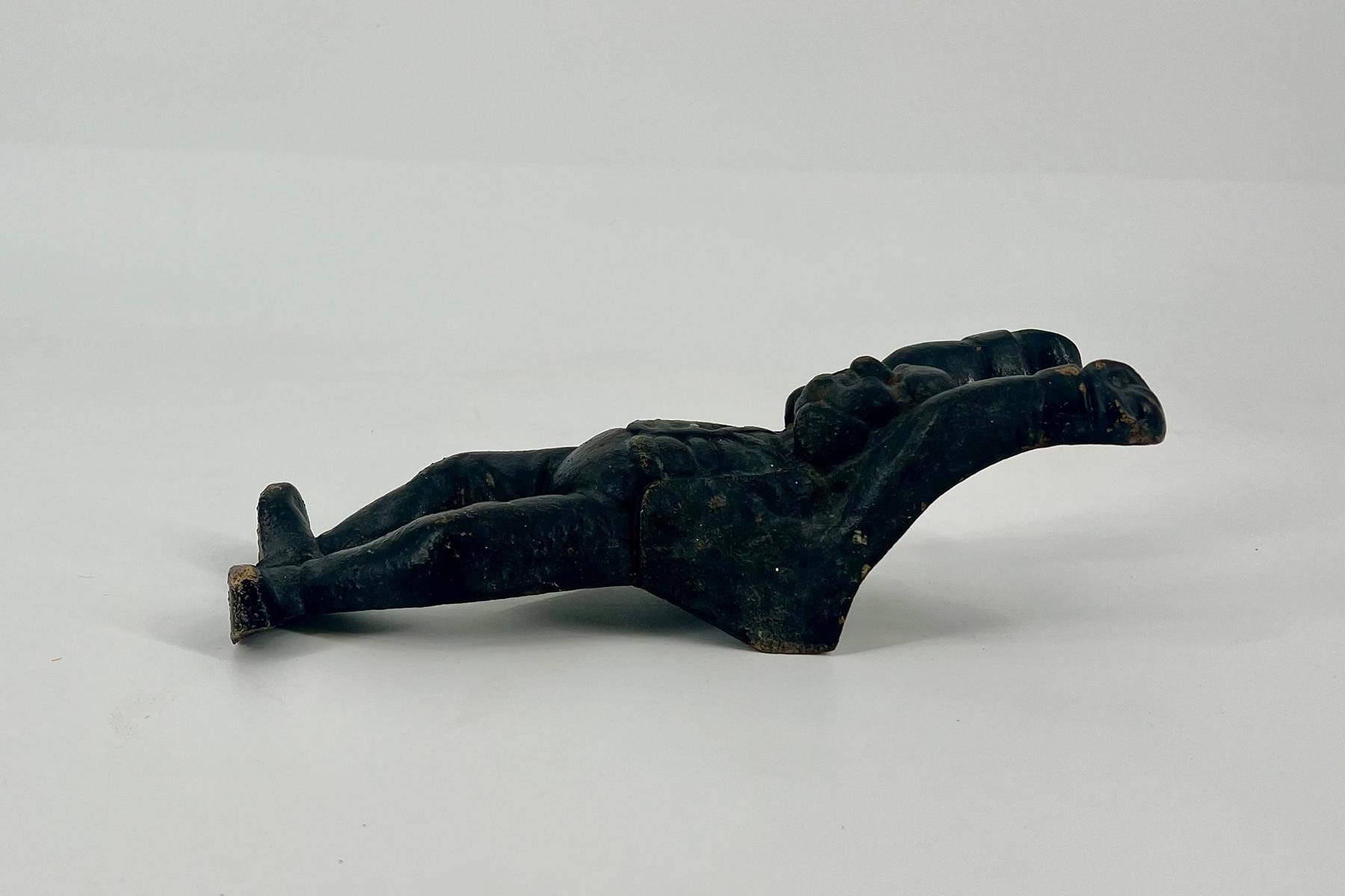 Dark patinated sculpture of a disembodied right hand resting on a light surface, viewed from the side.