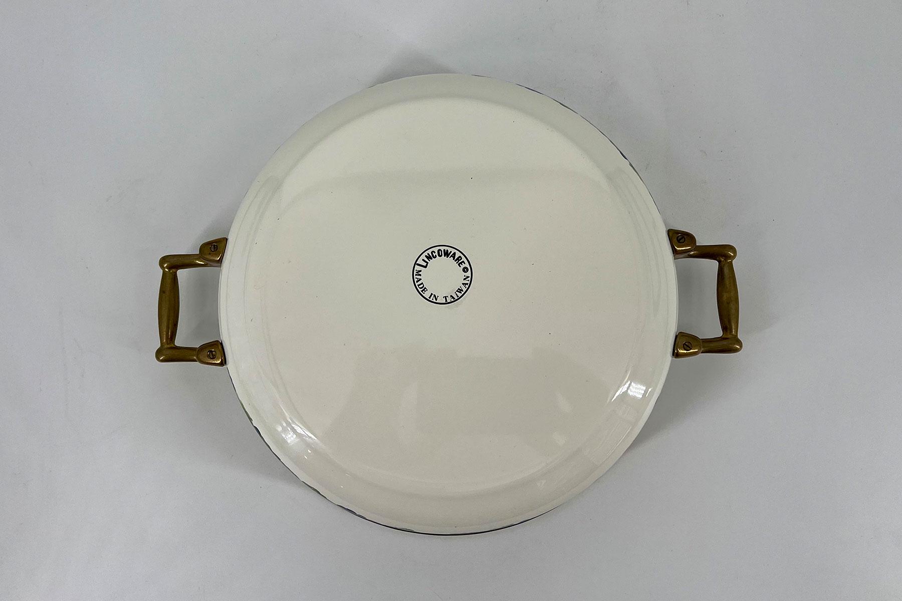 Top view of a white round ceramic serving dish with brown side handles; center circular maker's sticker says Made in Taiwan.