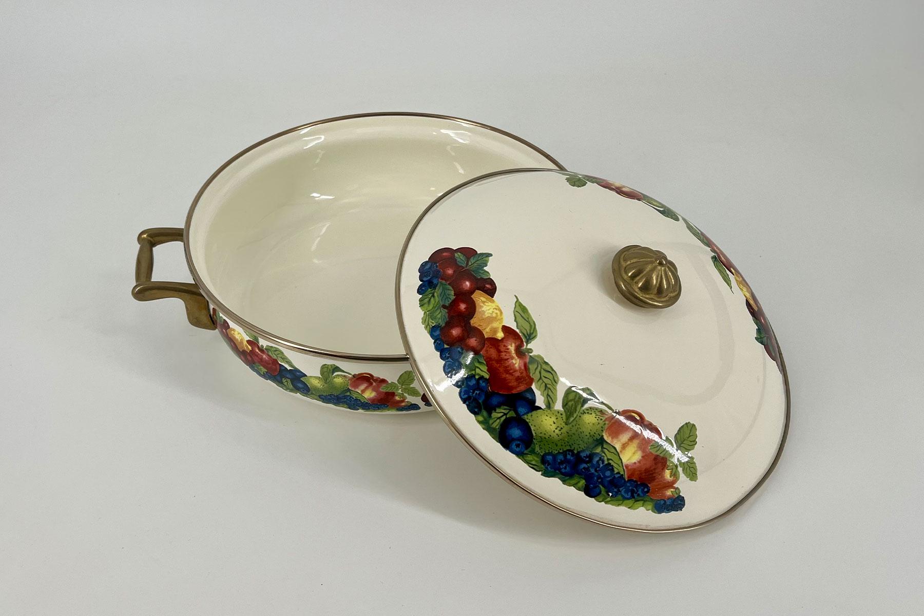 Decorative porcelain tureen with fruit pattern and brass handles, lid resting beside.