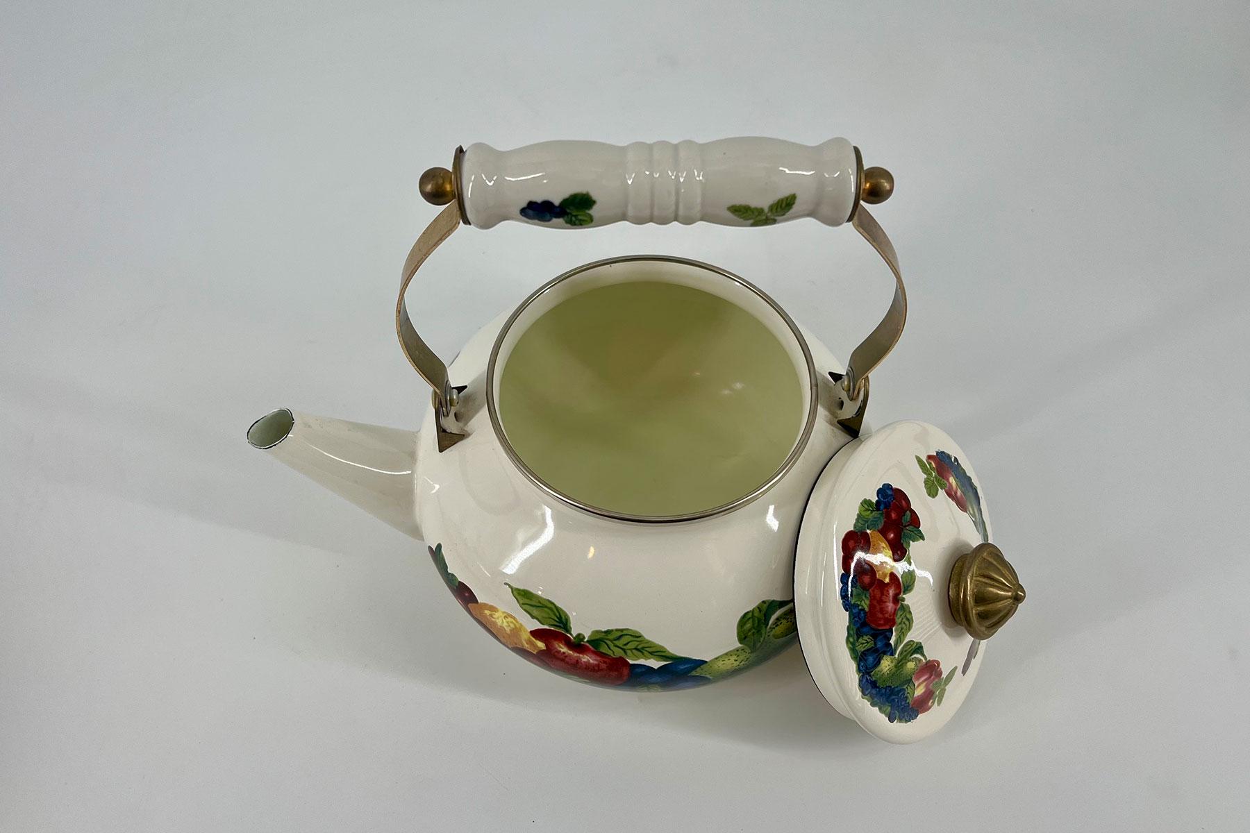 White porcelain teapot with colorful fruit and floral pattern; lid removed and placed to the side, handle upright over the pot.