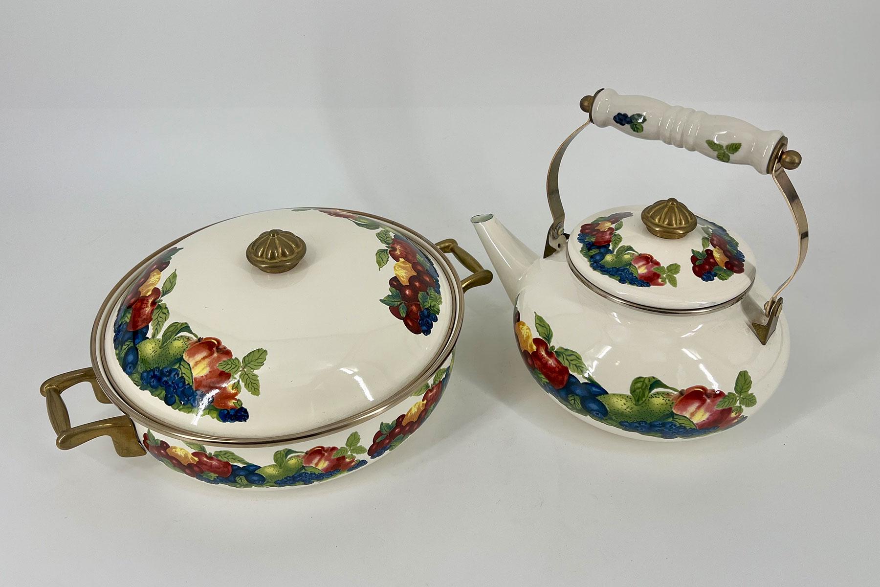 Two white ceramic teapots with brass trim and colorful fruit/flower grapevine decals, one with a lid and the other with a decorative handle.
