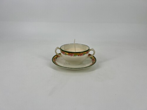 Teacup with floral border on a matching saucer, a single candle wick upright in the cup.