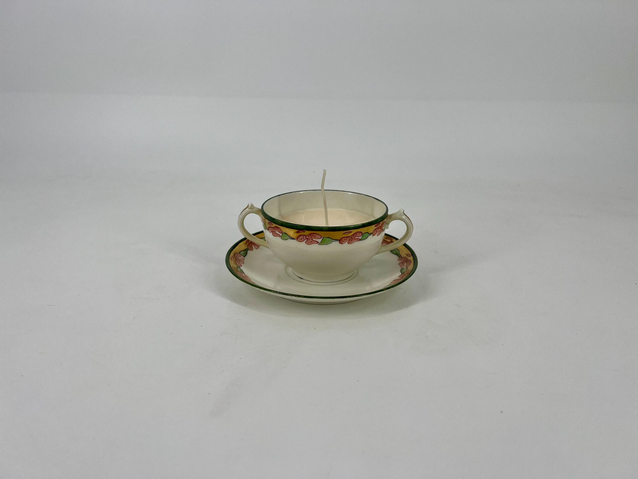 Teacup with floral border on a matching saucer, a single candle wick upright in the cup.