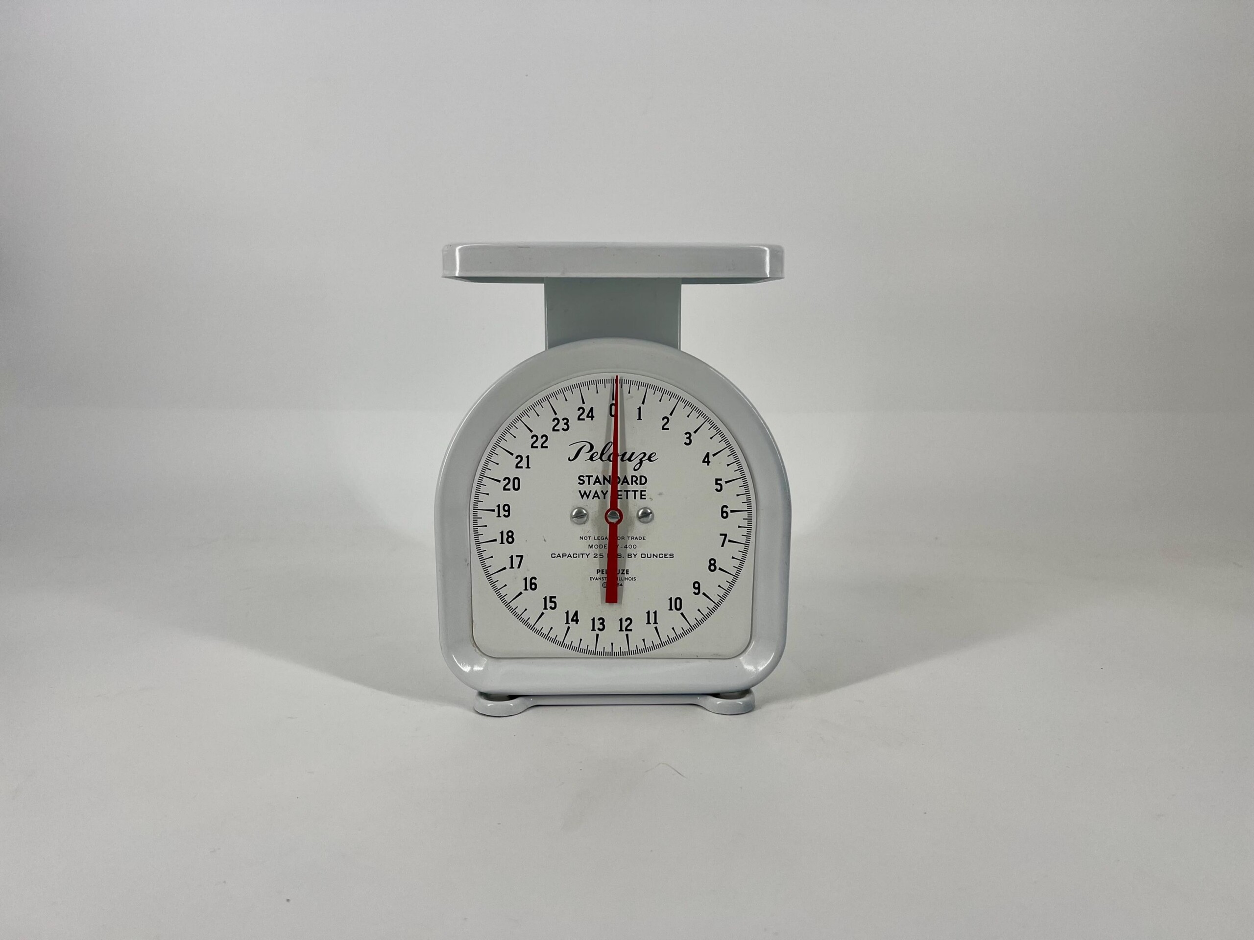 White vintage kitchen scale with a round dial and a flat top platform, showing weight indicators around the edge.