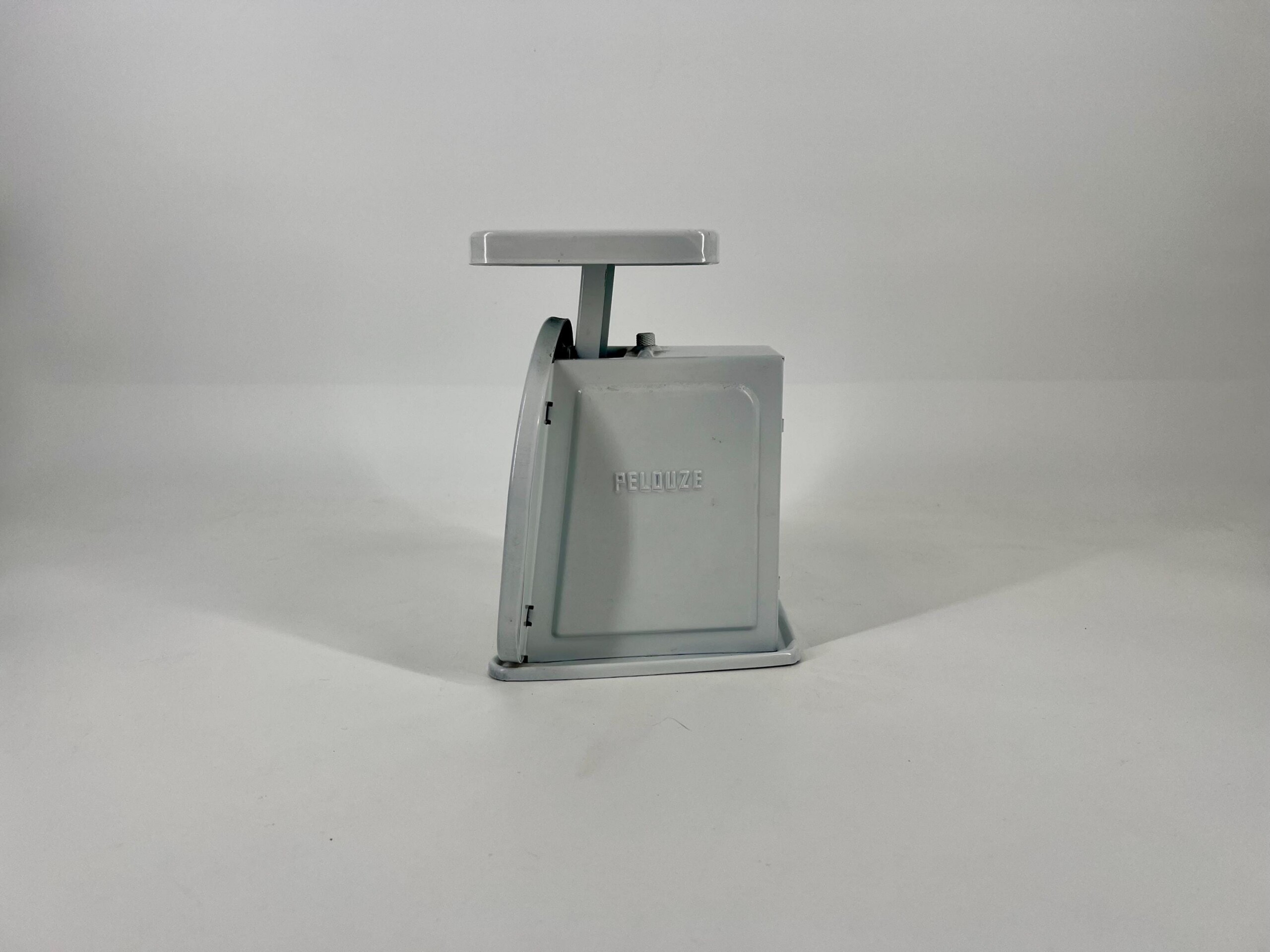 Gray vintage mechanical weighing scale with a flat rectangular tray on top and a vertical support, set against a plain light background.