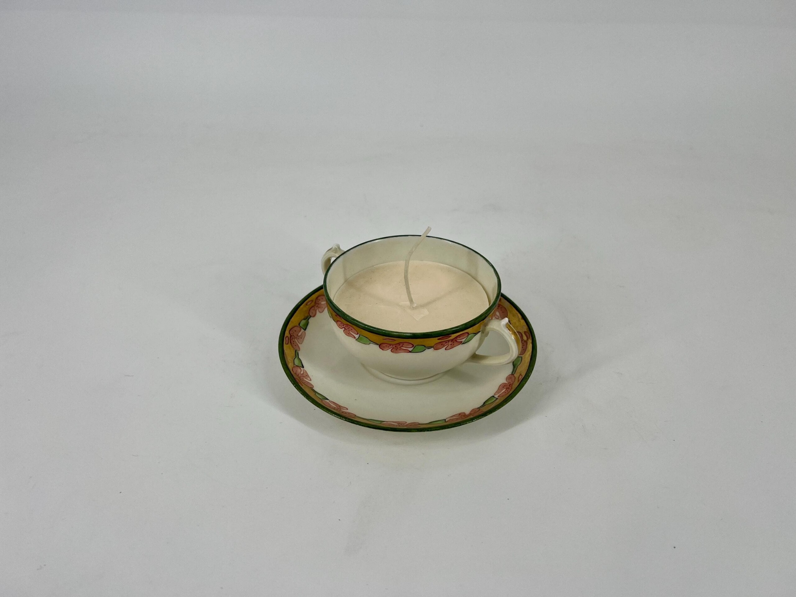 White ceramic teacup on a floral-patterned saucer with a candle burning inside the cup