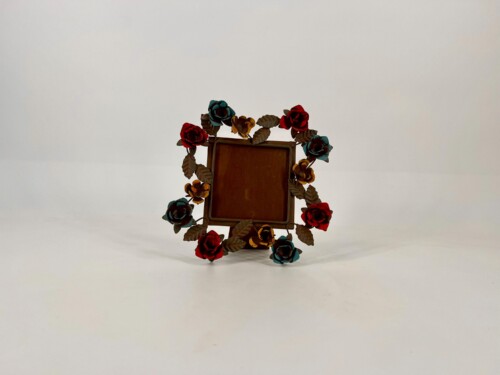 Brown rectangular frame surrounded by red, teal, and yellow paper roses and leaves against a pale background.
