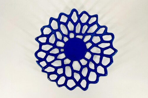 Blue decorative lattice disc with petal-like openings on a white background (flower-like perforated plate). The object resembles a sunburst pattern.