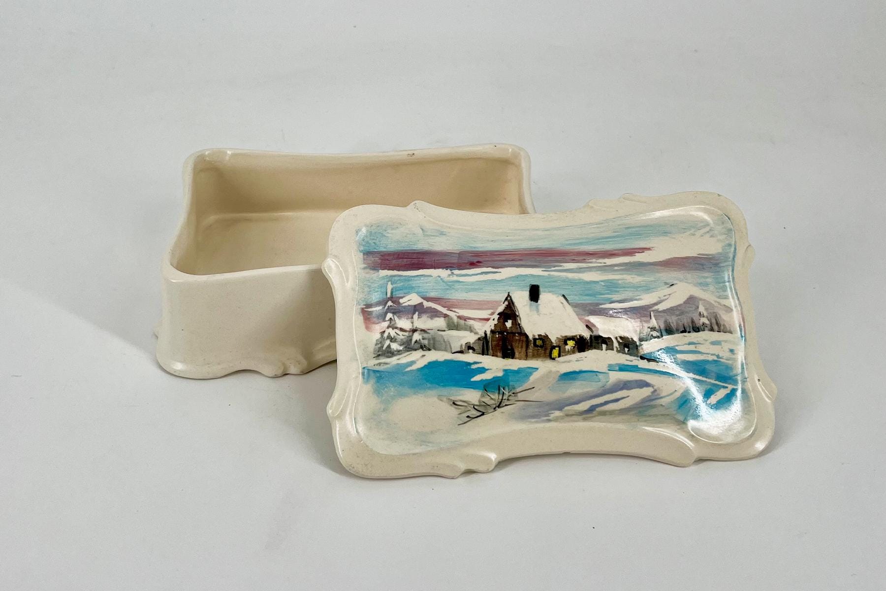 Ceramic lidded box with a hand-painted snowy village scene on the lid and a cream interior.