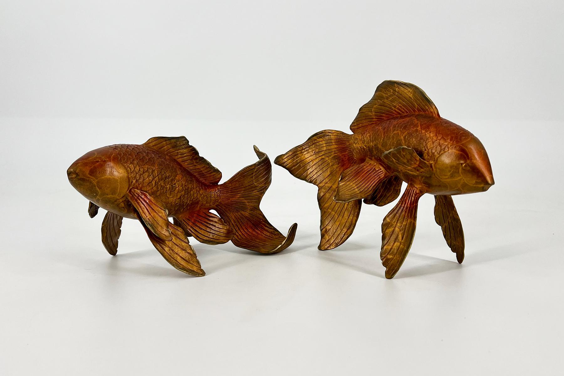 Two carved wooden goldfish sculptures in amber tones, with flowing fins, arranged on a white surface facing opposite directions.