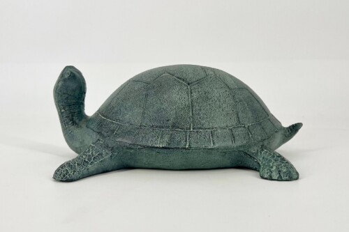 Teal-green turtle figurine with a segmented shell resting on a white surface, facing left.