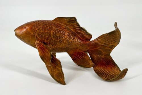 Wooden carved fish sculpture with detailed scales and flowing tail fins facing left.