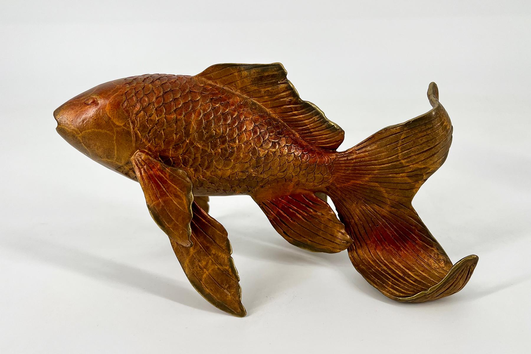 Wooden carved fish sculpture with detailed scales and flowing tail fins facing left.