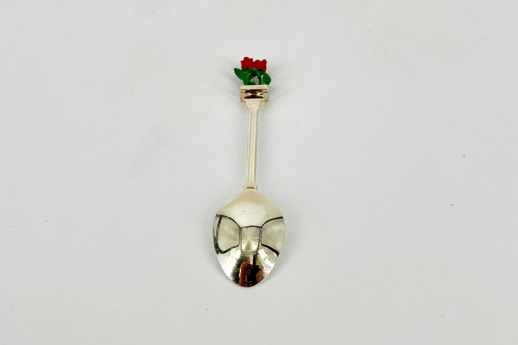Silver spoon with a skull-shaped bowl and a small red rose blooming at the top of the handle.