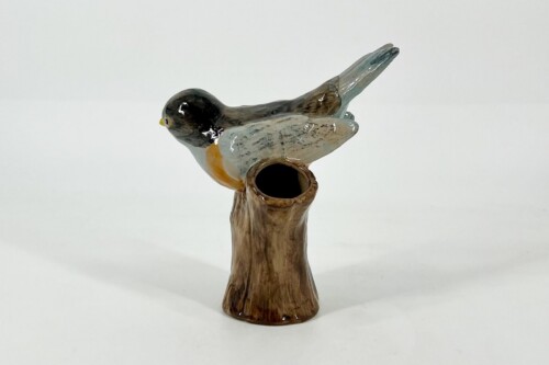 Glazed ceramic bird perched on a brown vase-like stand with a hollow opening in the top.