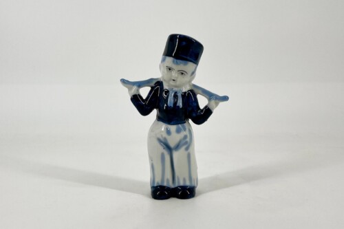 Ceramic figurine of a person in blue and white clothing with a tall black hat, arms outstretched.
