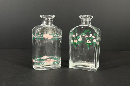 Two clear glass bottles with pink floral bands and green leaves, set on a black background.