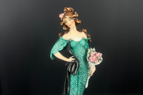 Ceramic figurine of a woman in a green, off-the-shoulder dress holding a pink bouquet.
