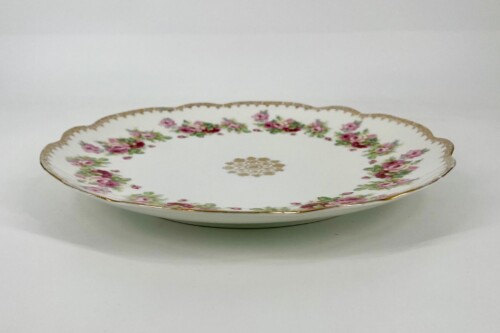 Decorative porcelain plate with a pink rose border and a gold trim along the scalloped edge, on a white background.