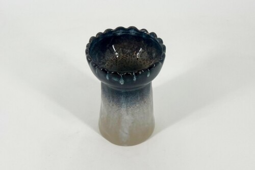 Dark blue scalloped ceramic bowl sits on a bottle neck against a white background, glaze slightly glossy and drippy at the rim.
