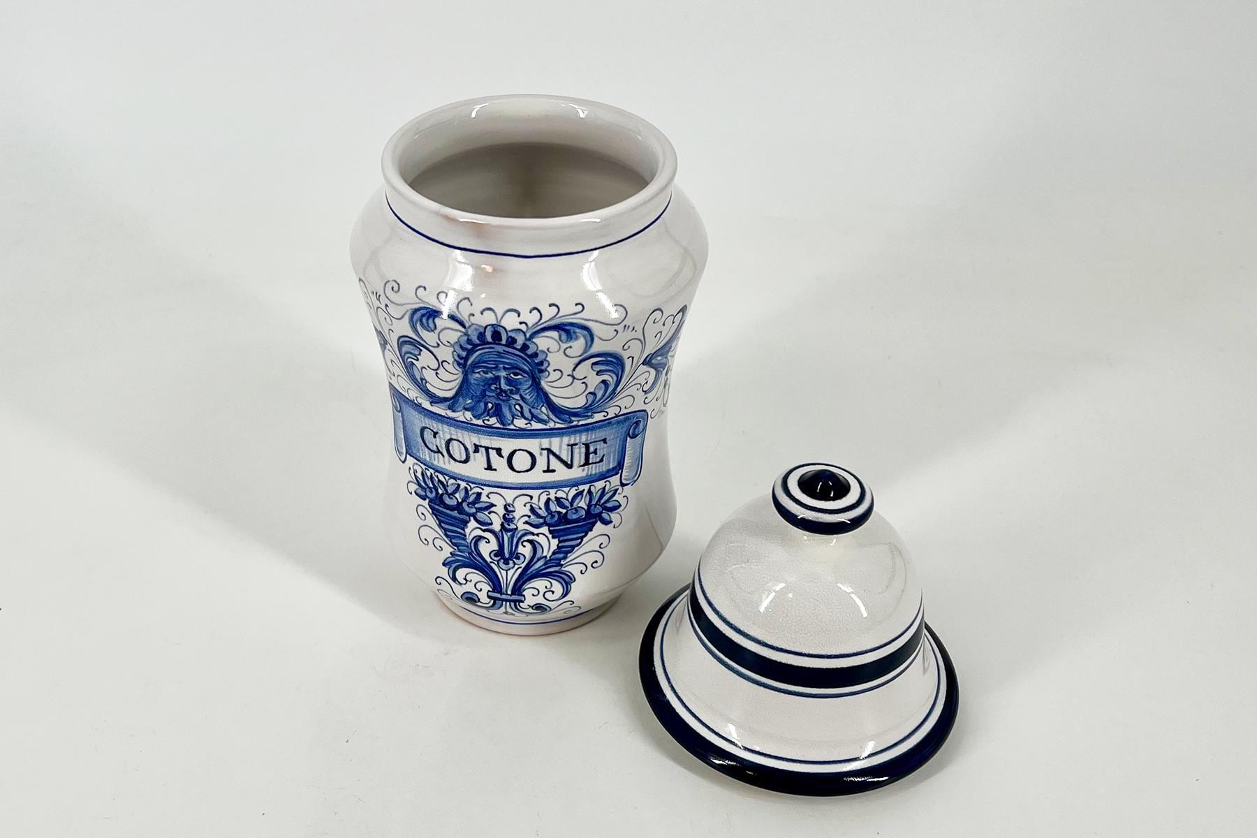 White ceramic jar with blue floral scrollwork and the word 'COTONE' on a banner, paired with matching blue-rimmed lids beside it.