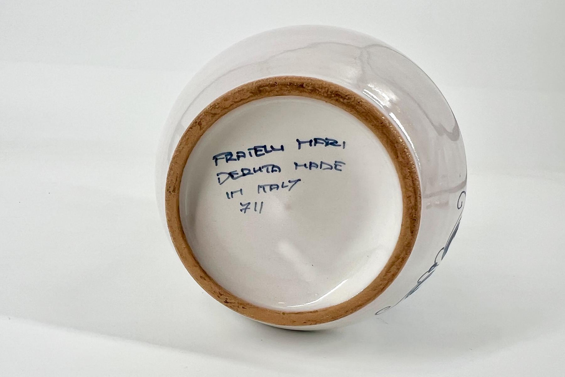 Bottom of a white ceramic cup with a tan unglazed foot ring and blue handwritten inscription on the base.